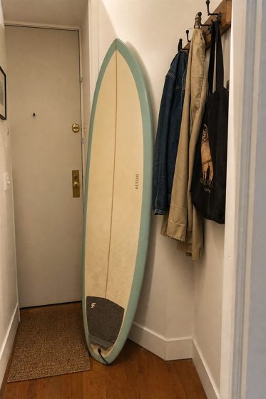 The reference photo: a pale surfboard leaning in a hallway by the front door.